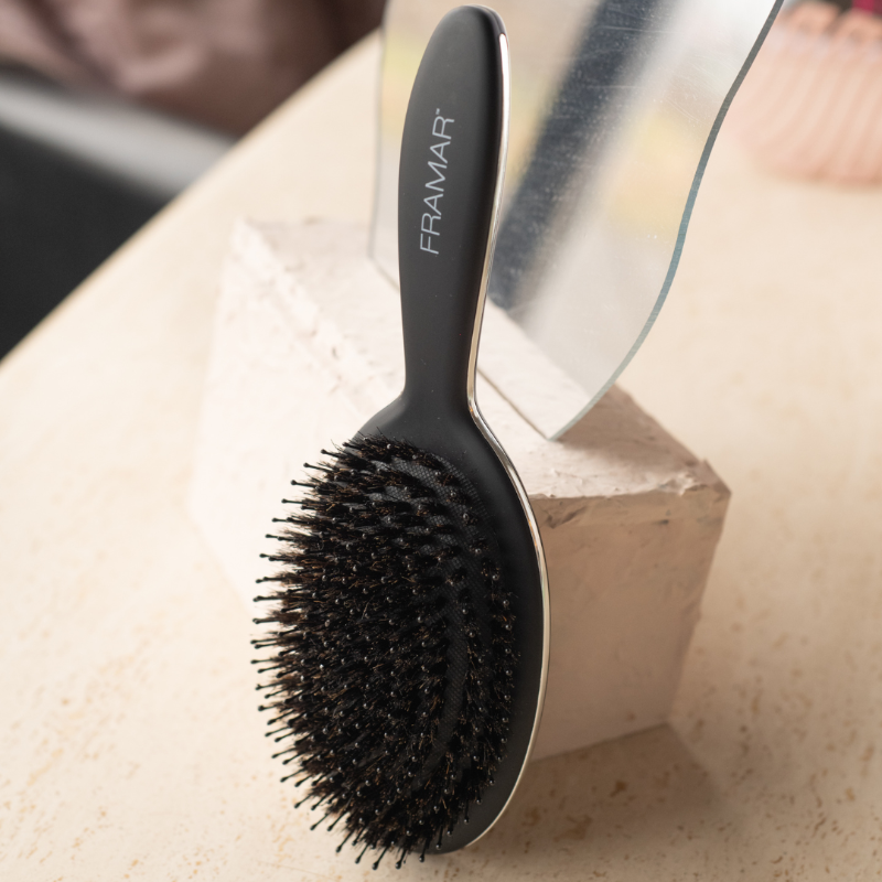 The back of the Framar Polish Brush resting on a salon display block showing its sleek black design