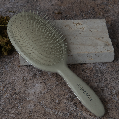 Framar professional detangling brush in sage green resting on a stone block