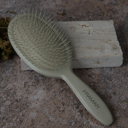 Framar professional detangling brush in sage green resting on a stone block