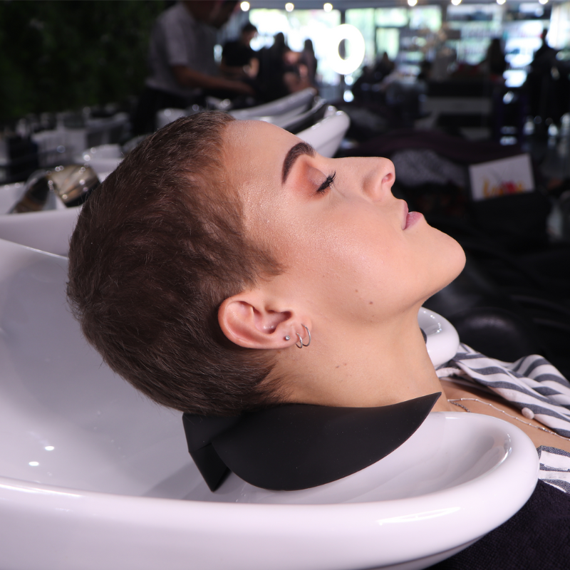 Female client resting comfortably on a black HeadBed neck cushion at a white salon shampoo basin