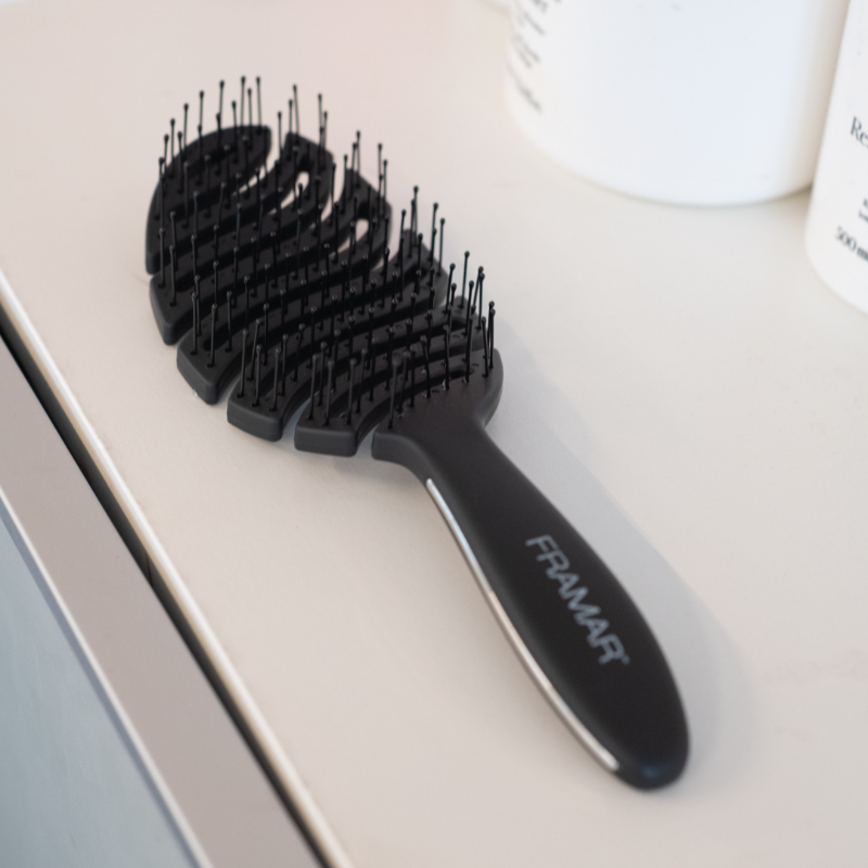 Matte black professional vented detangling brush resting on a salon workstation